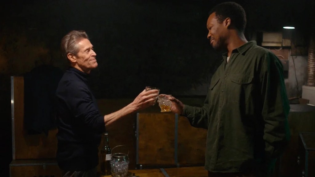 Willem Dafoe and Corey Hawkins clink drinks in a dark room